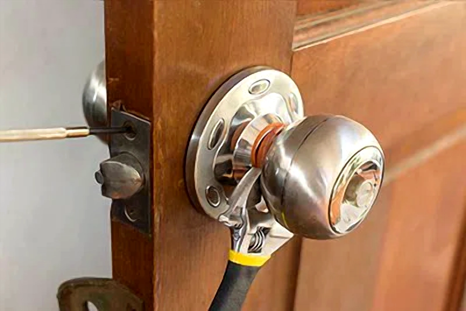 Locksmith repairing a residential doorknob and latch mechanism with hand tools.